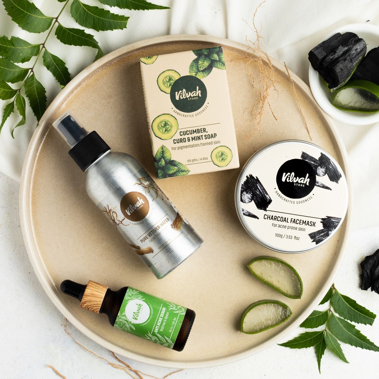 Flat lay of natural skin care products featuring charcoal facemask, cucumber soap, and essential oils on a light surface