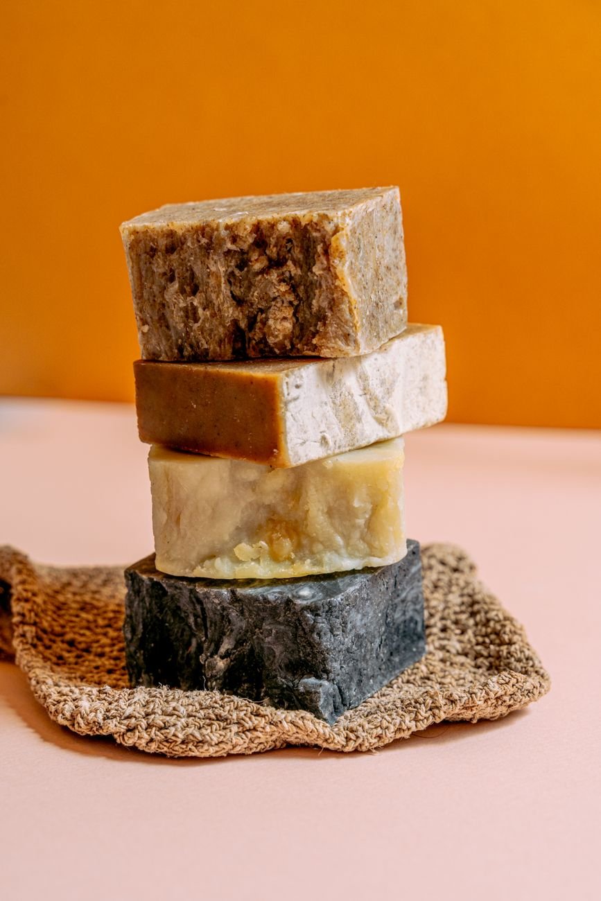 Four handmade natural soap bars stacked on a textured mat against a warm background